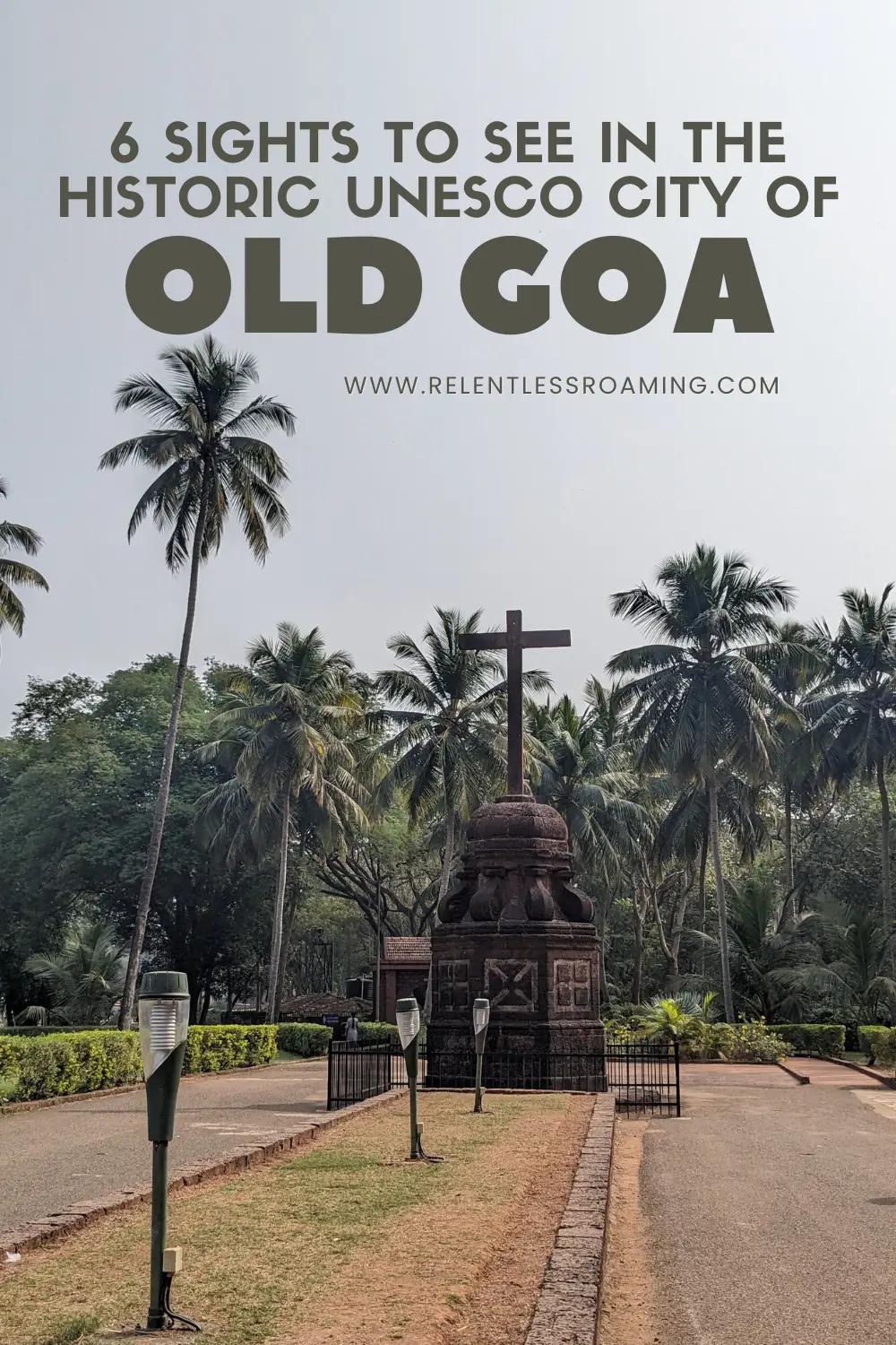 a cross with a short top sits on a brick pedestal surrounded by palm trees in Old Goa