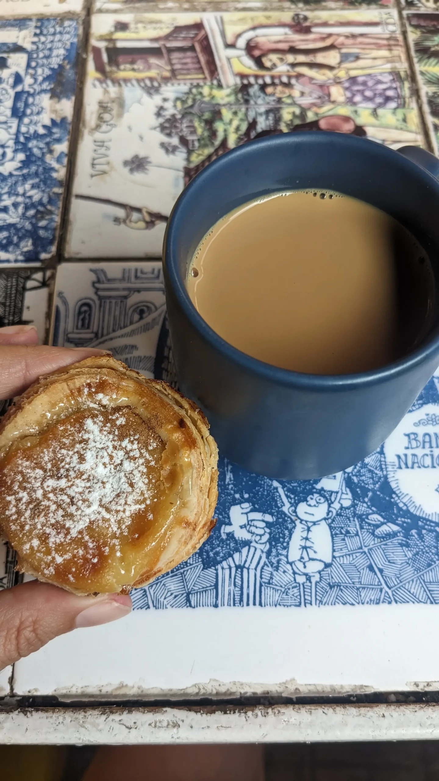 Pastel de nata and masala chai a close up of a small pastel de nata and a blue mug of masala chai sat on a tiled table in Confeitaria 31 de Januario