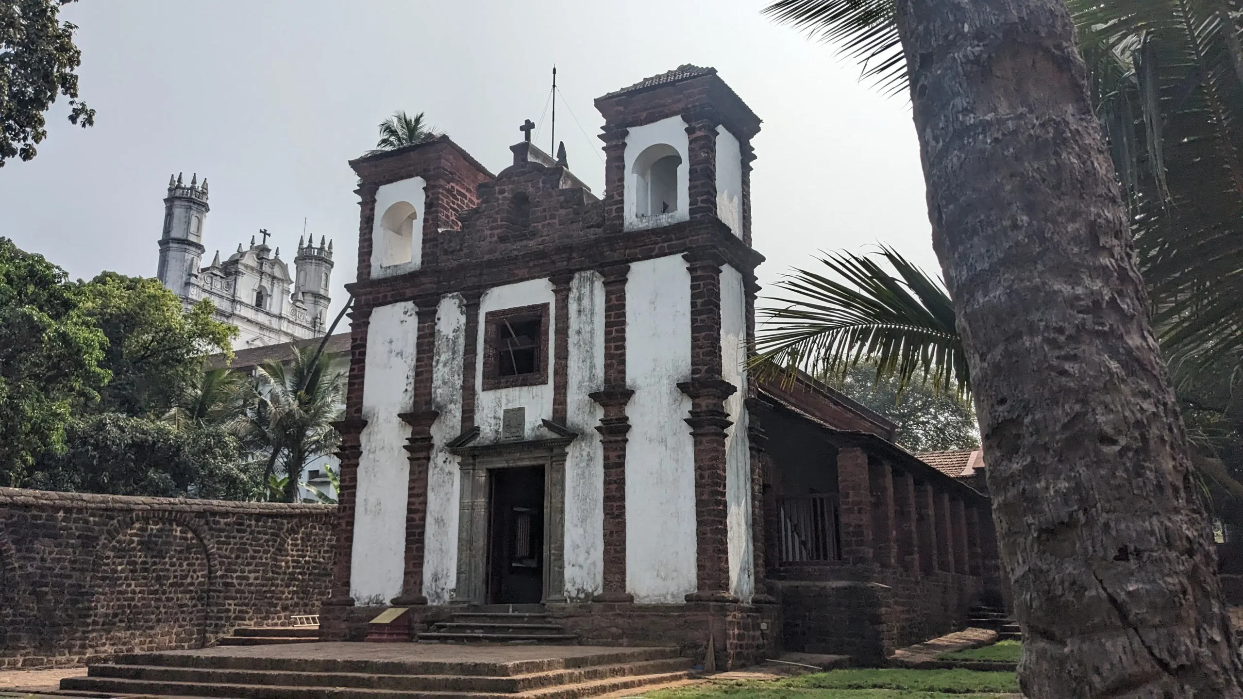 a white and red brick facade of the chapel of St Catherine is surrounded by palm trees in Old Goa
