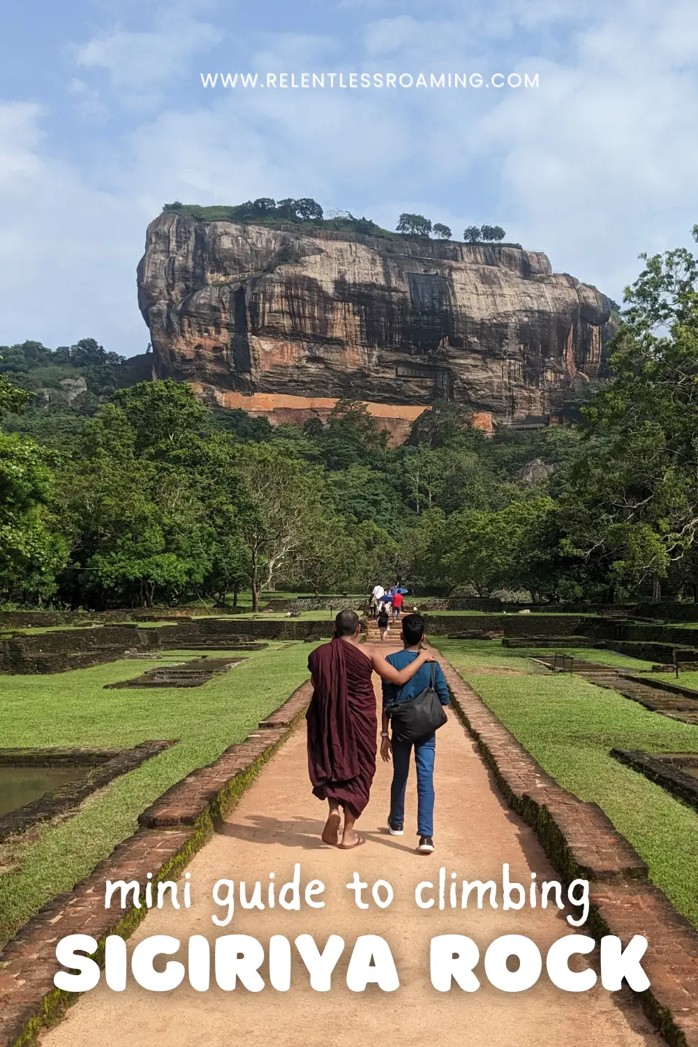 a paved walkway surrounded by maintained gardens leads towards the huge granite rock of Sigiriya Rock.