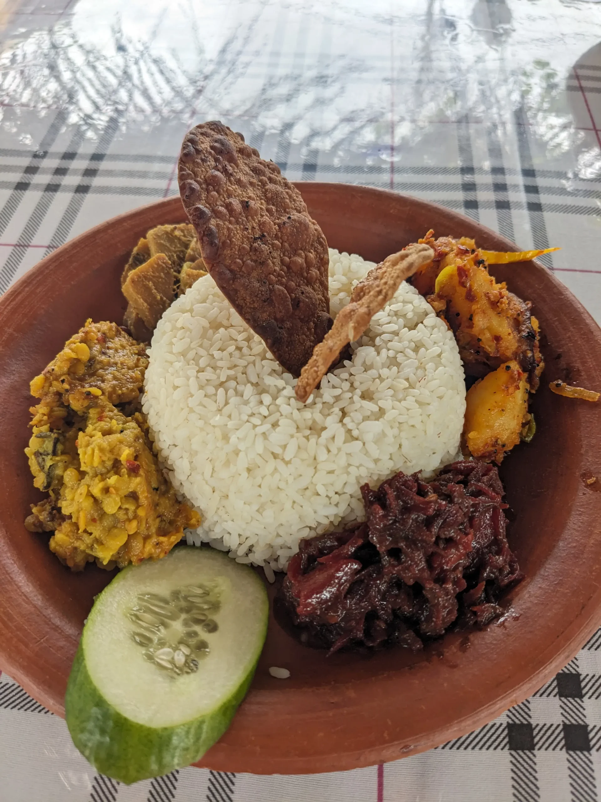 Rice and curry a mound of white rice sits int he centre of a clay bowl, surrounded by four thick vegetable curries - spicy potato, beetroot, dal, and breadfruit. There is a slice of cucumber and two crisp papads. Sri Lankan rice and curry