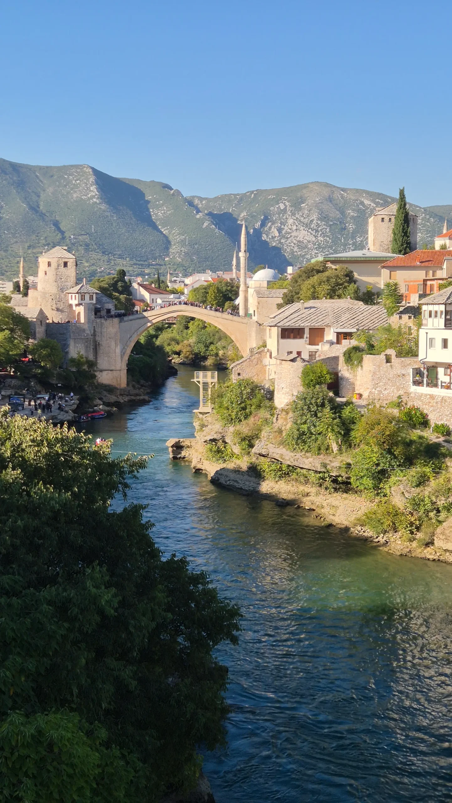 the Ottoman-style stone arched bridge (Stari Most) stands above the Neretva river with traditional Ottoman buildings, towers, minarets either side. Mostar, Bosnia and Herzegovina