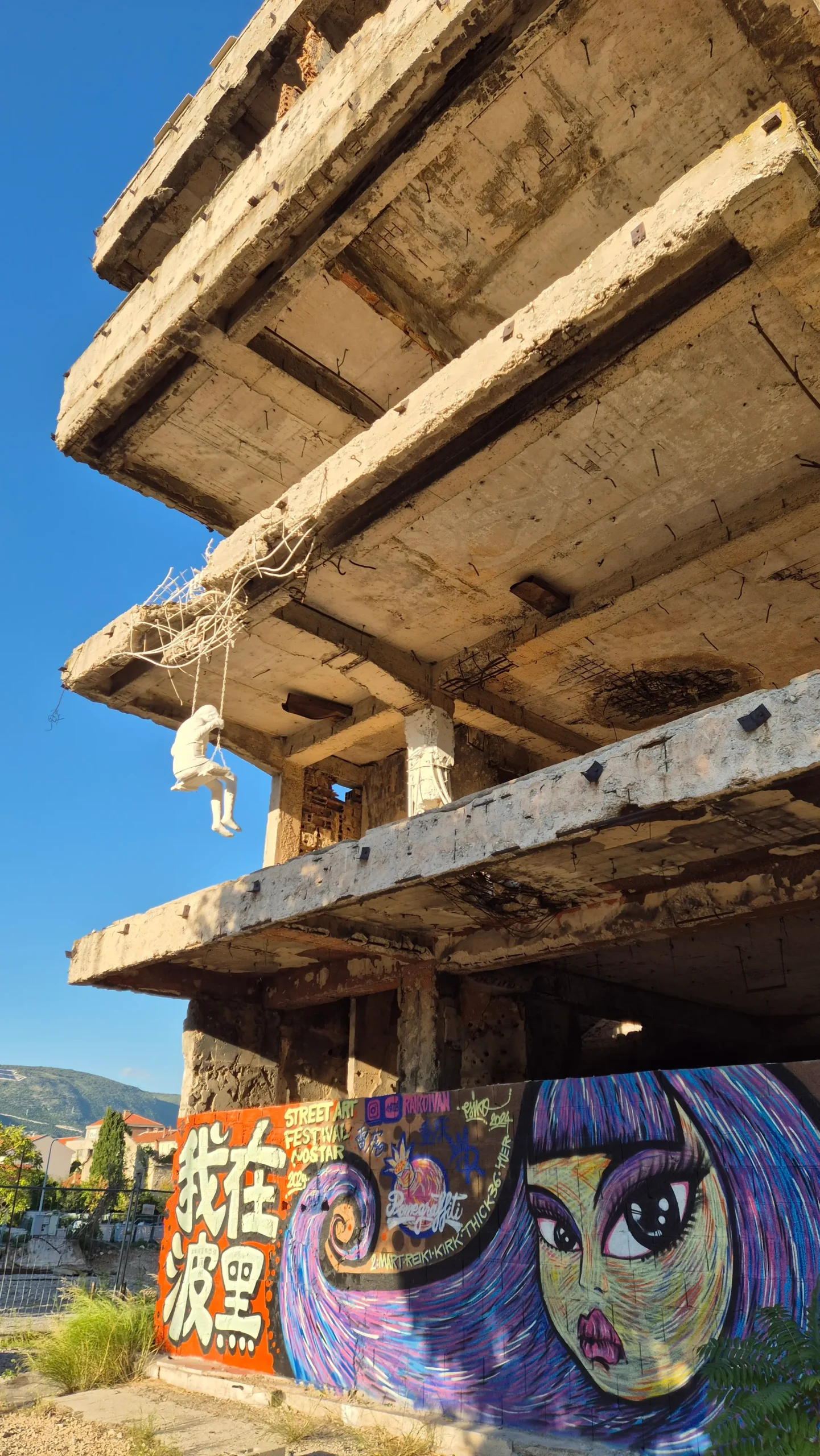 an art installation on a heavily-bombed building near the frontline of the Bosnian War in Mostar, shows a human figure sat on a swing painted in white.