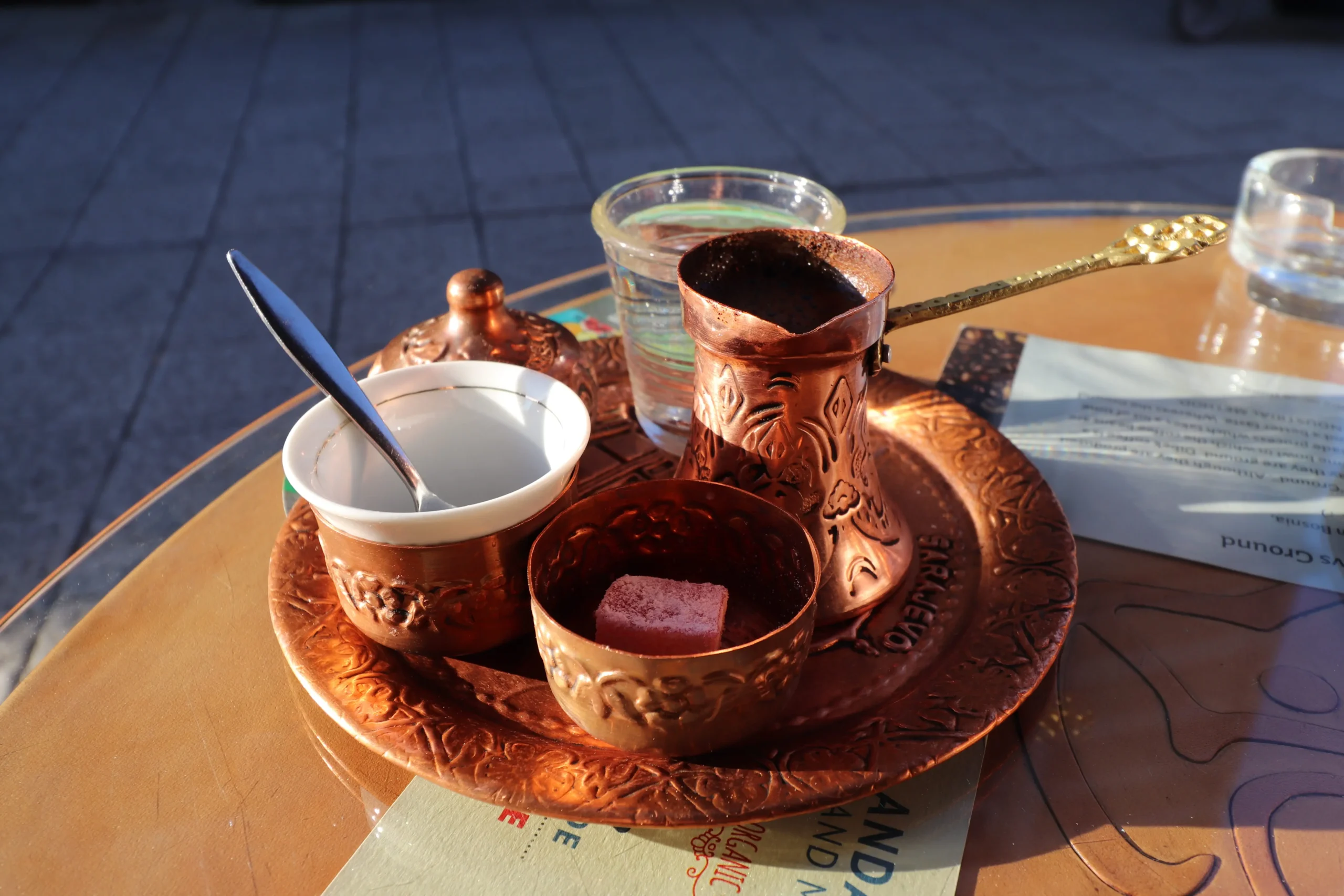 a traditional Bosnian coffee set of a copper plate with a copper coffee pot with a long handle, a small pot for sugar cubes, a small pot for lokum, a small glass of water and a small coffee cup. Sarajevo, Bosnia and Herzegovina