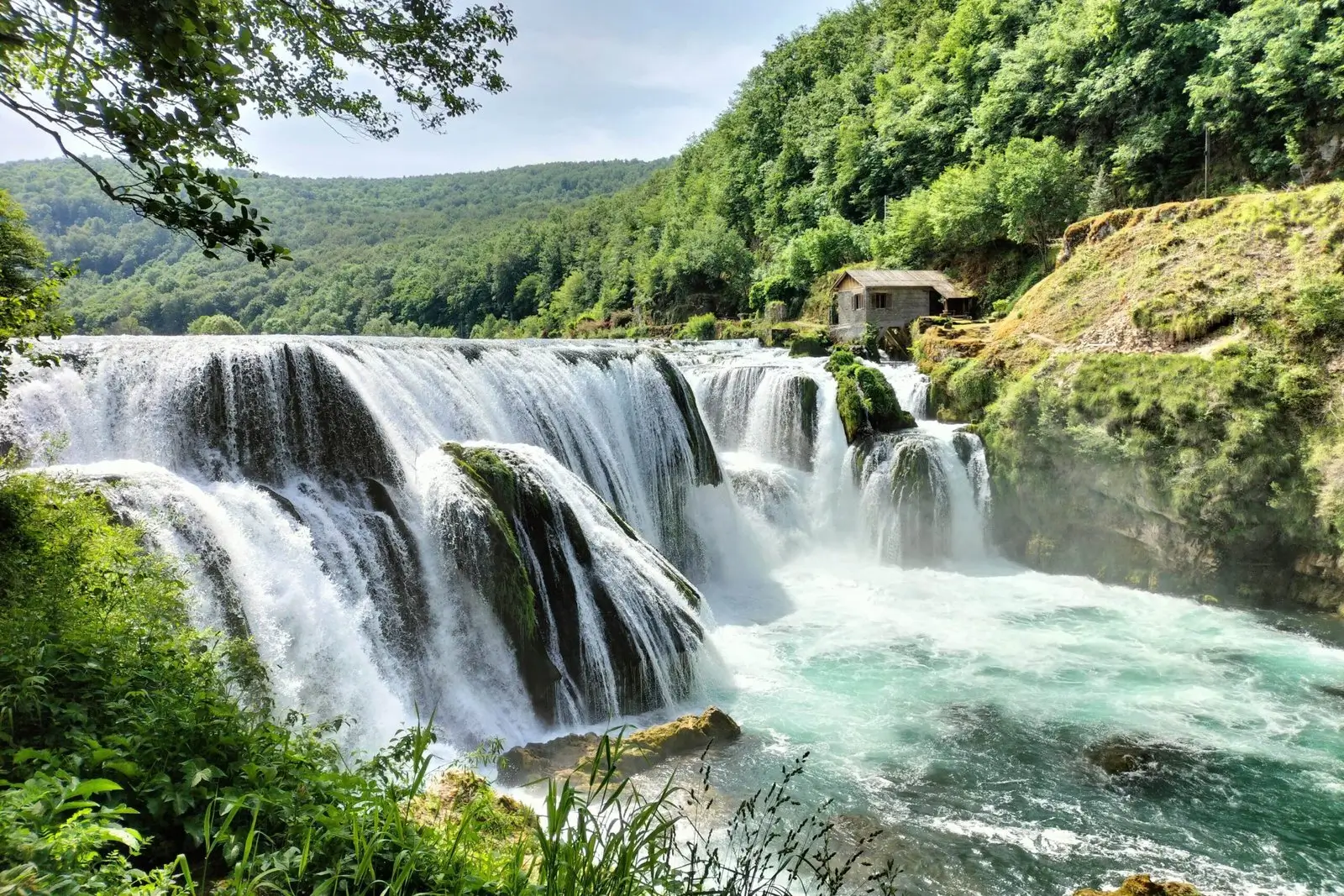 a photo of Štrbački Buk waterfall shows water plummeting down to a plunge pool with a green, forested backdrop. Una National Park. Travel tips for Bosnia and Herzegovina