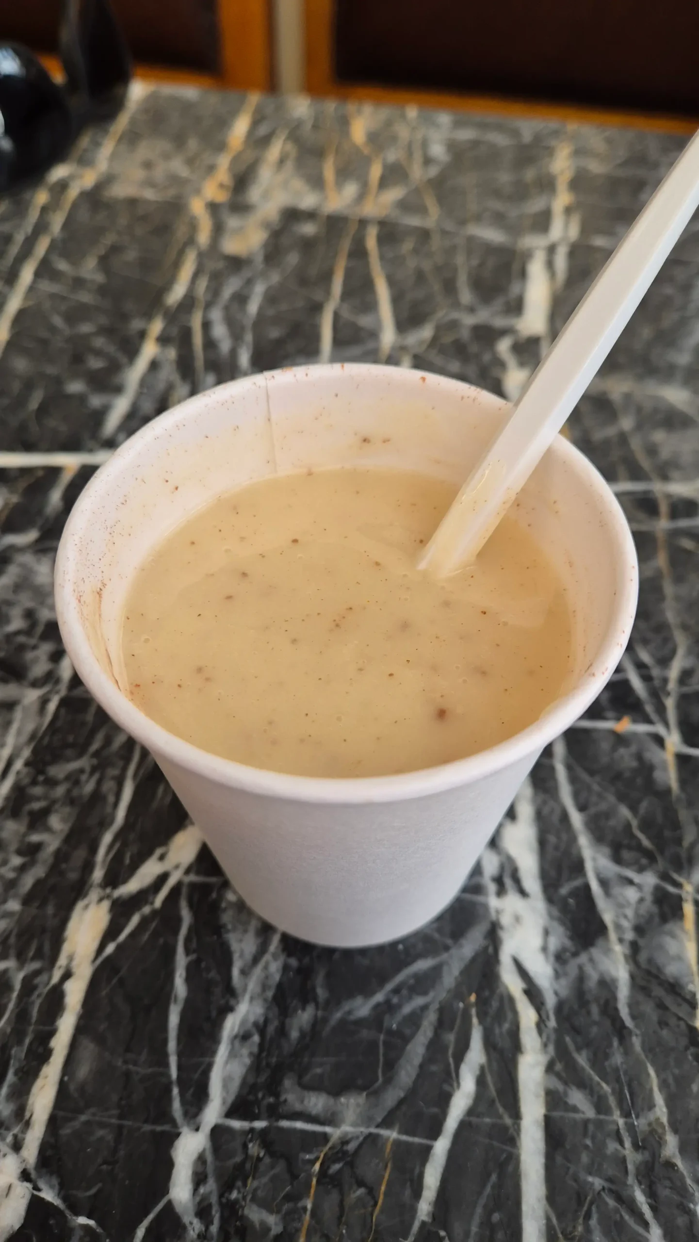 boza boza - a white paper cup is filled with what looks like a thick custard sprinkled with cinnamon