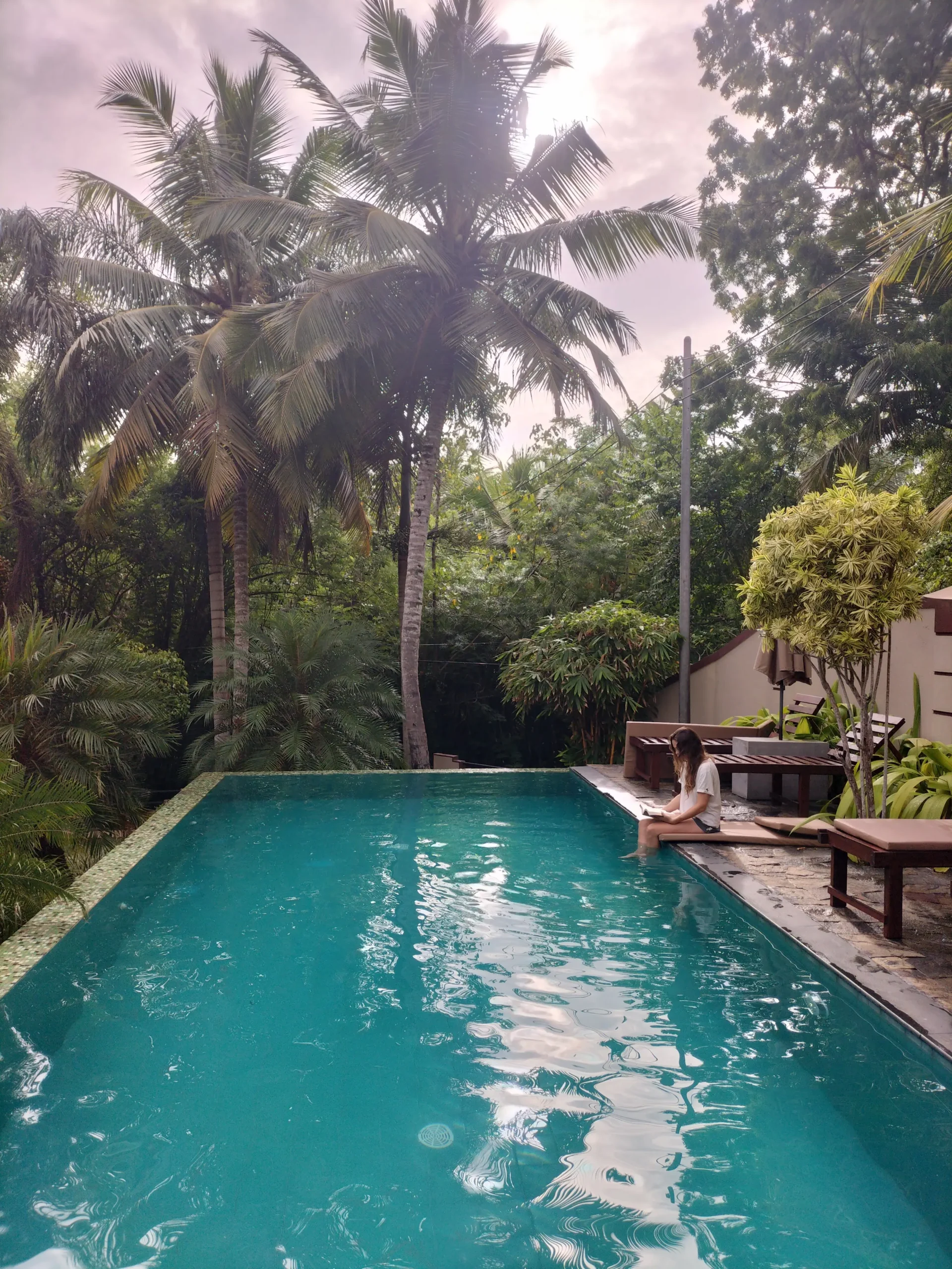 Goyambokka Guesthouse Pool a woman sits at a rectangular pool dangling her feet in the water as she reads a book. the pool is surrounded by tropical plants at Goyambokka Guesthouse, Sri Lanka