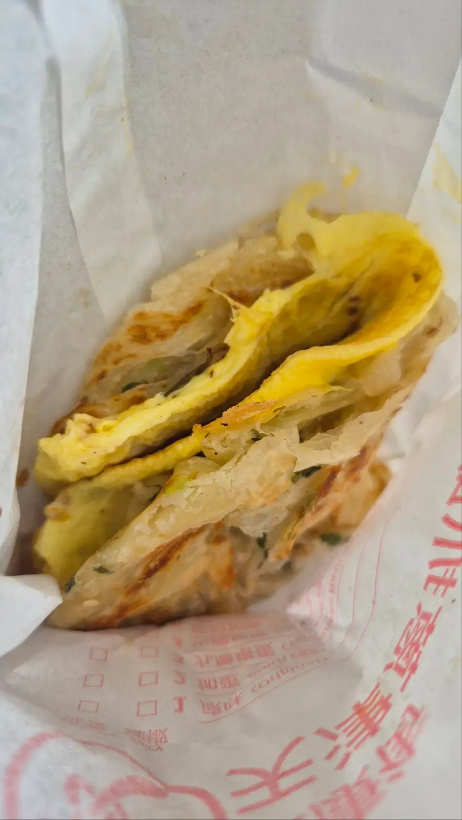 a paper bag has a flaky Taiwanese scallion pancake with omelette