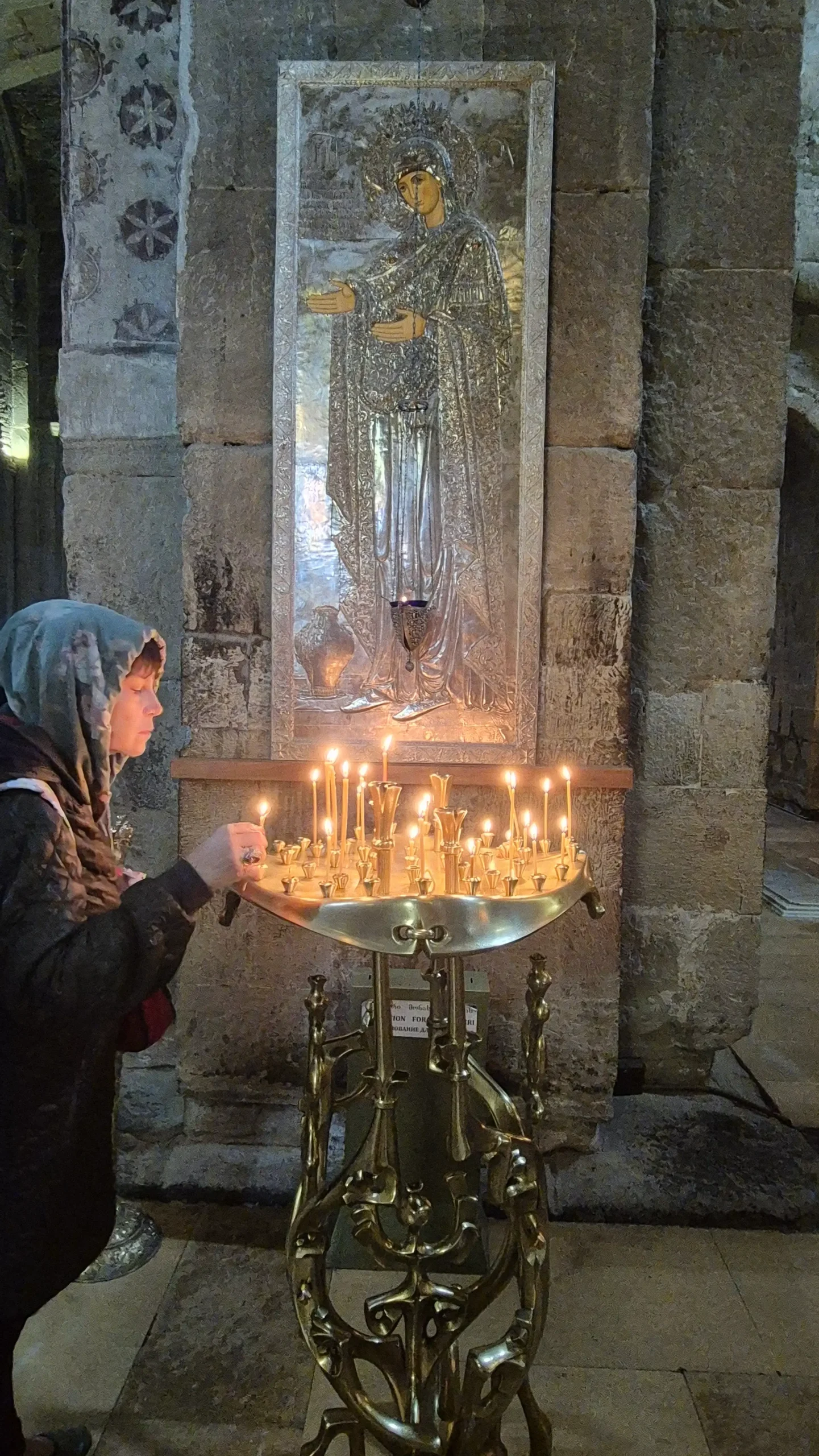 a woman places a lit candle on a stand in front of artwork depicting a religious figure in Svetitskhoveli Cathedral, Mtskheta, Georgia