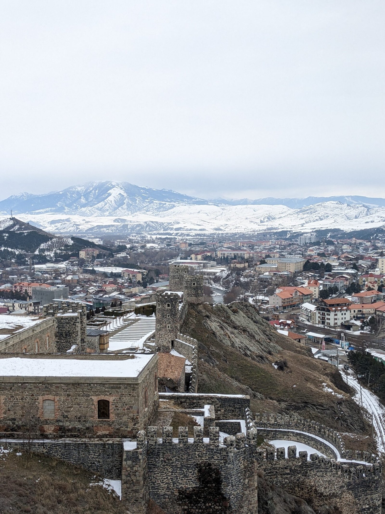 a view from Rabati Castle shows fortress walls and towers, Akhaltsikhe town, and mountains covered in snow in Georgia