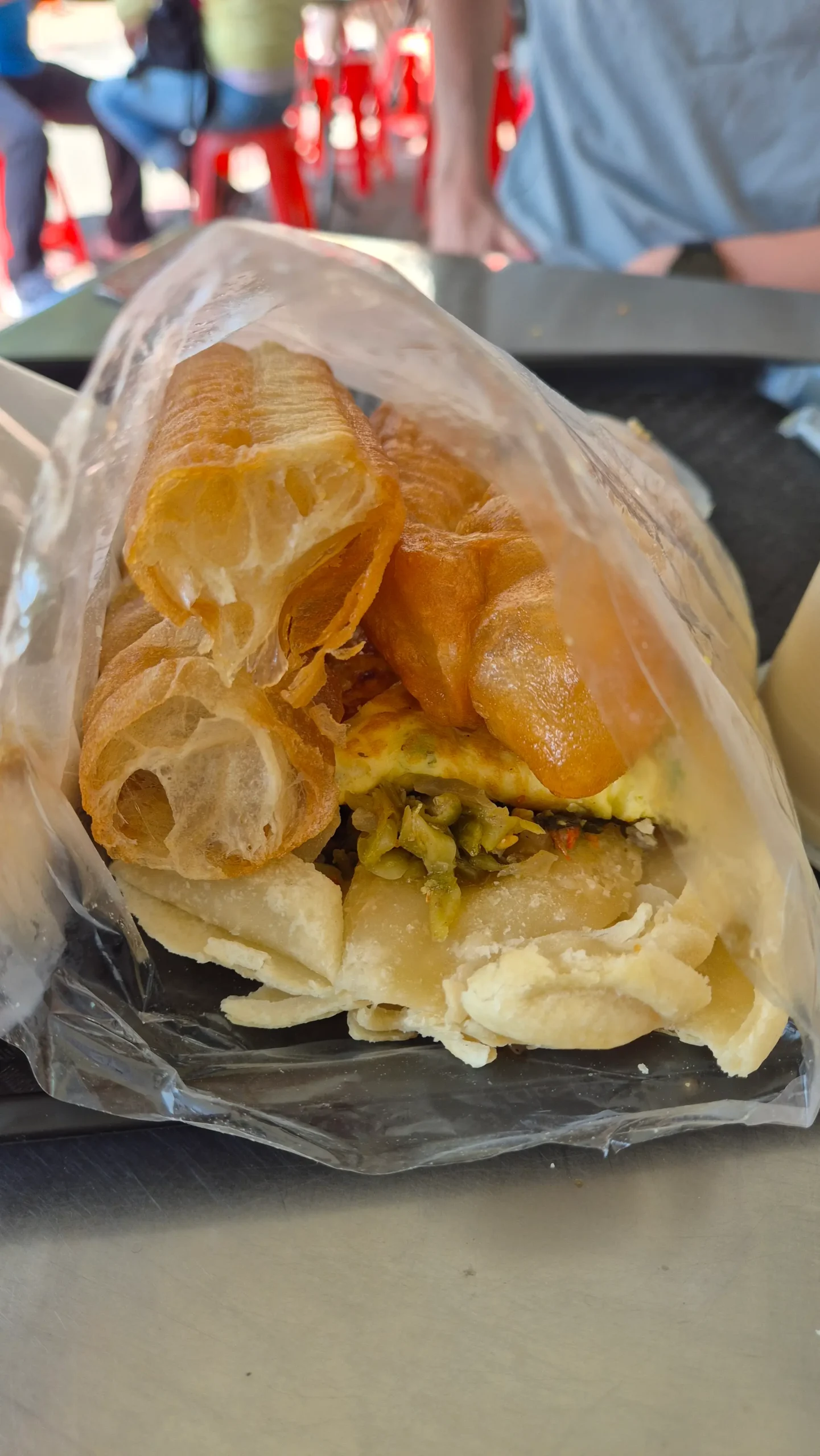a flaky sesame bread (shaobing) has long savoury doughnuts (youtiao), pickled mustard greens, and scallion omelette inside - Taiwanese breakfast