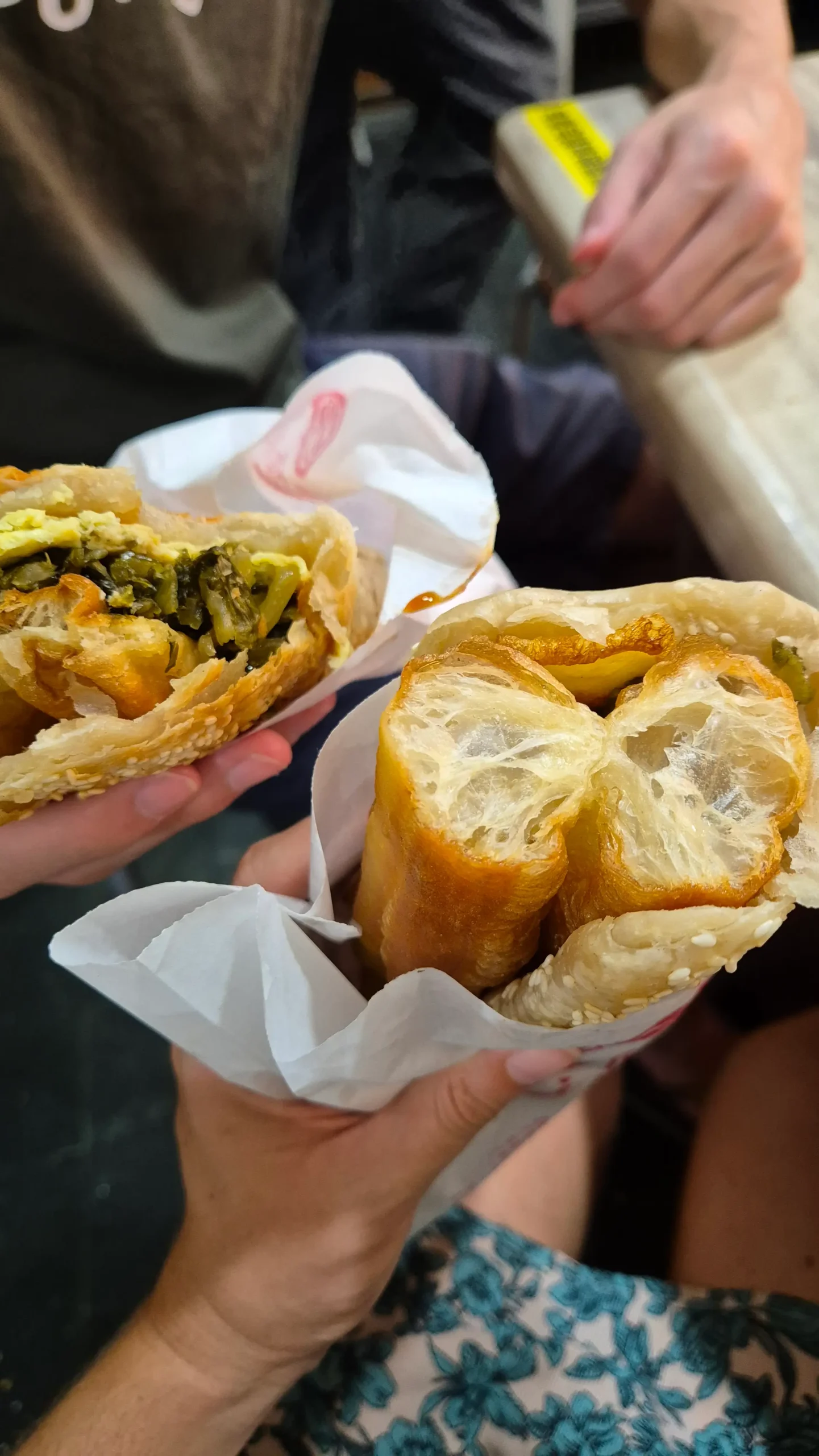 a flaky sesame bread (shaobing) has long savoury doughnuts (youtiao), pickled mustard greens, and scallion omelette inside - Taiwanese breakfast