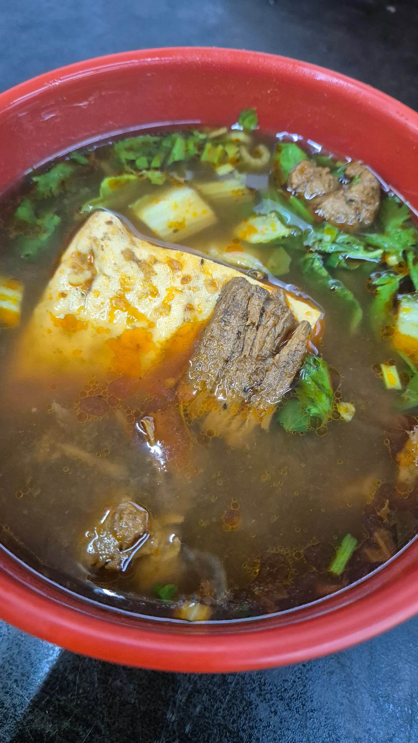 a red bowl has a brown broth with vegetarian 'meat', a block of stinky tofu, coriander, and cabbage in Tainan, Taiwan