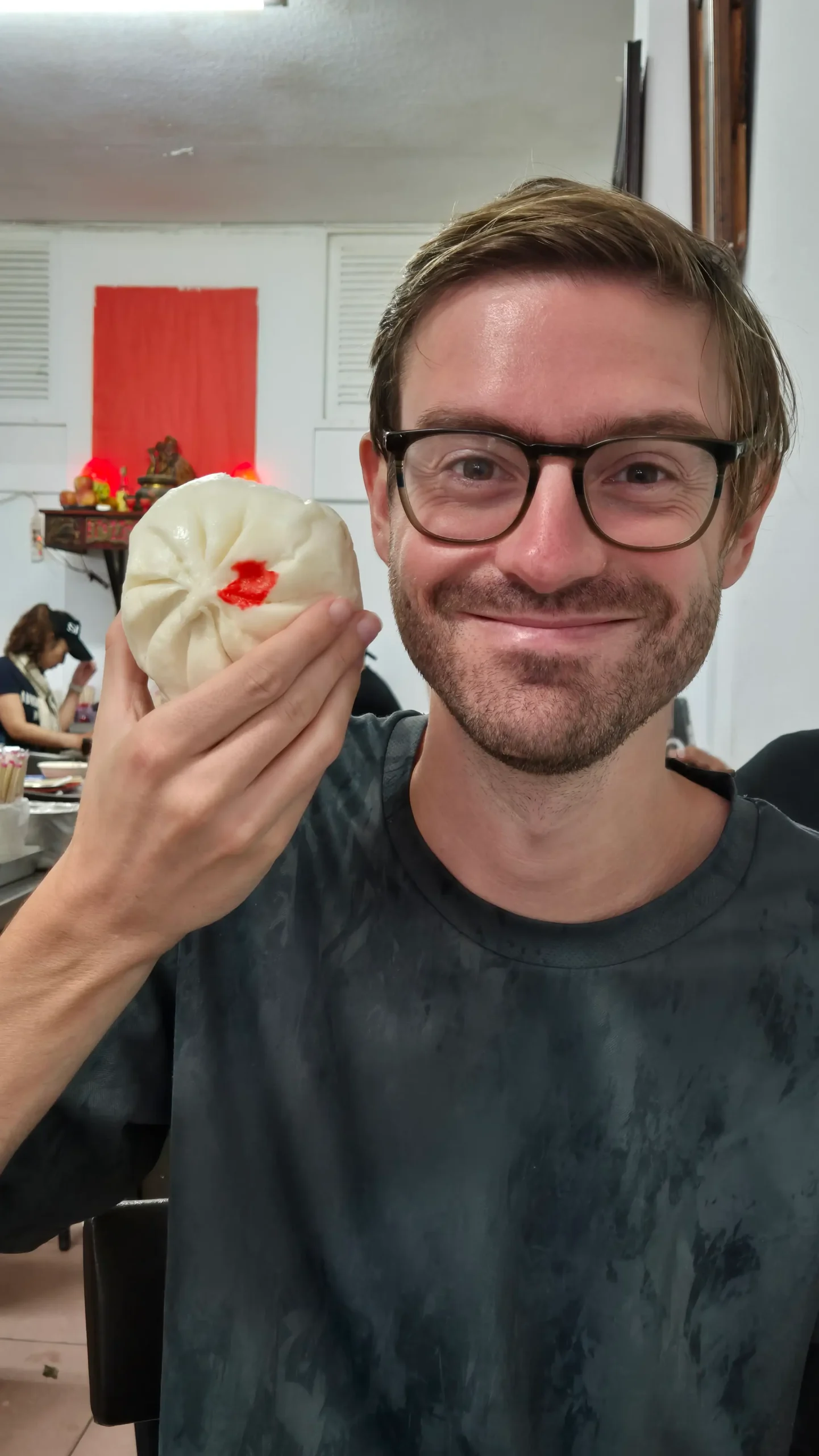 a man holds up a steamed bun to show the huge size of it compared to his head.