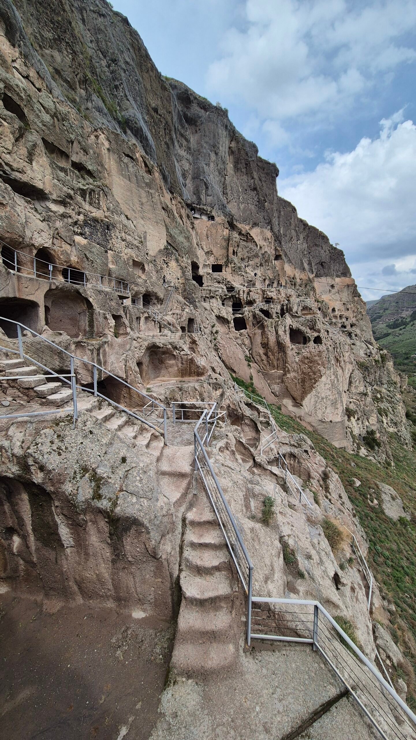 the exterior of the ancient cave city of Vardzia shows worn staircases, passageways and rooms carved into the rockface