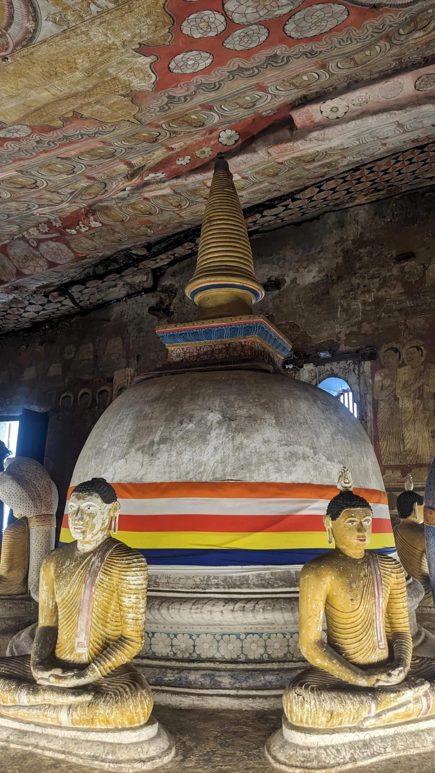 seated Buddha statue sit around a white bell-shaped dagoba decorated with a Buddhist flag inside Dambulla Cave Temple