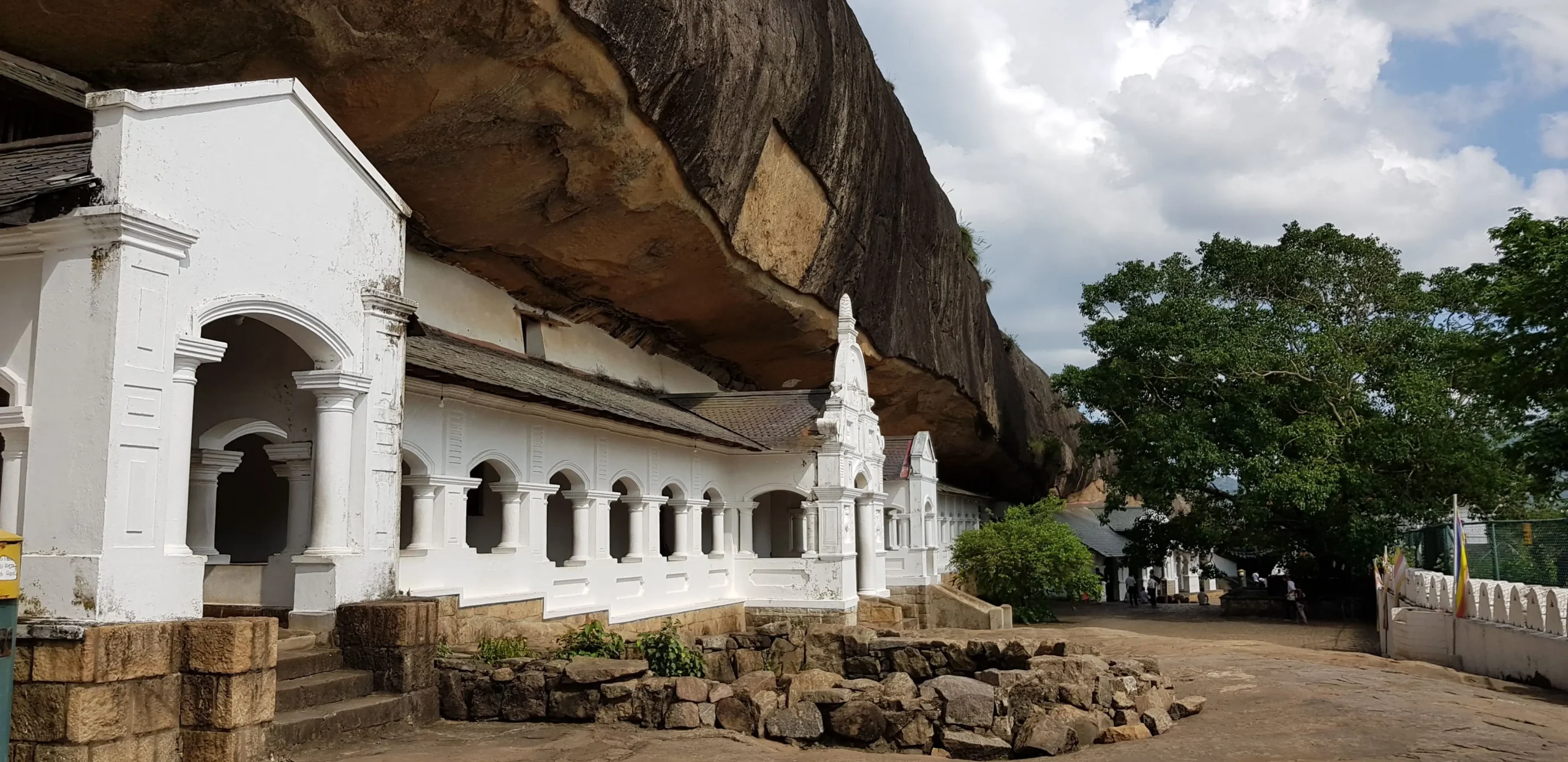 Dambulla Cave Temple has a white facade built into a rock face with a large rock overhang