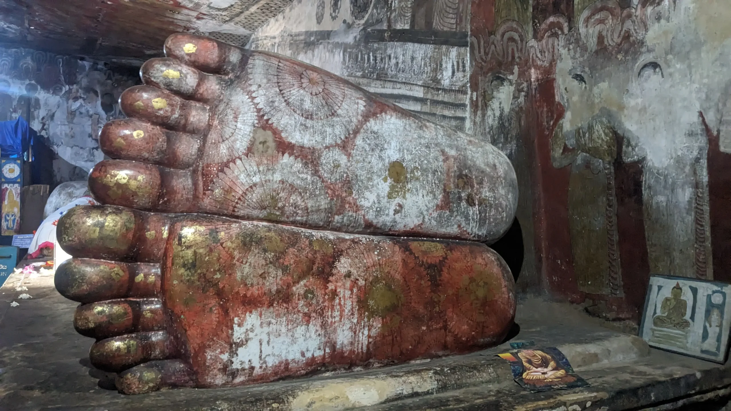 the underside of the feet of a large reclined Buddha statue are decorated with red, white and gold flowers in Dambulla Cave Temple