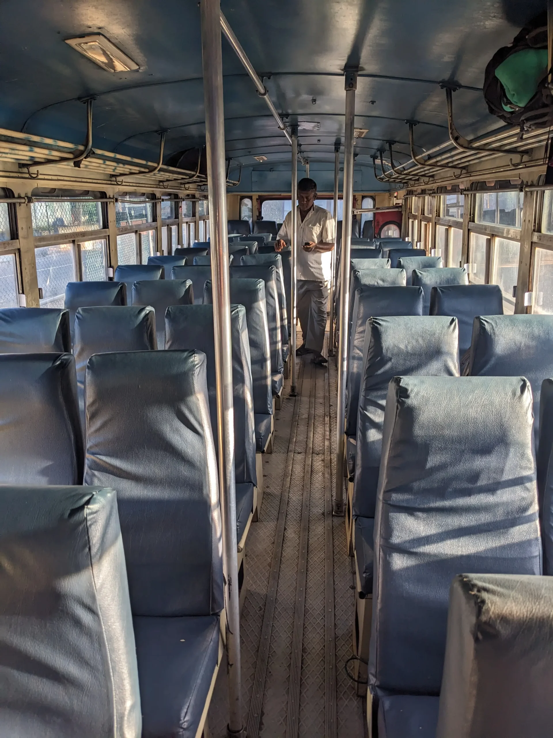 the interior of a Sri Lankan bus shows two rows of seats, an aisle and metal bag storage above the seats