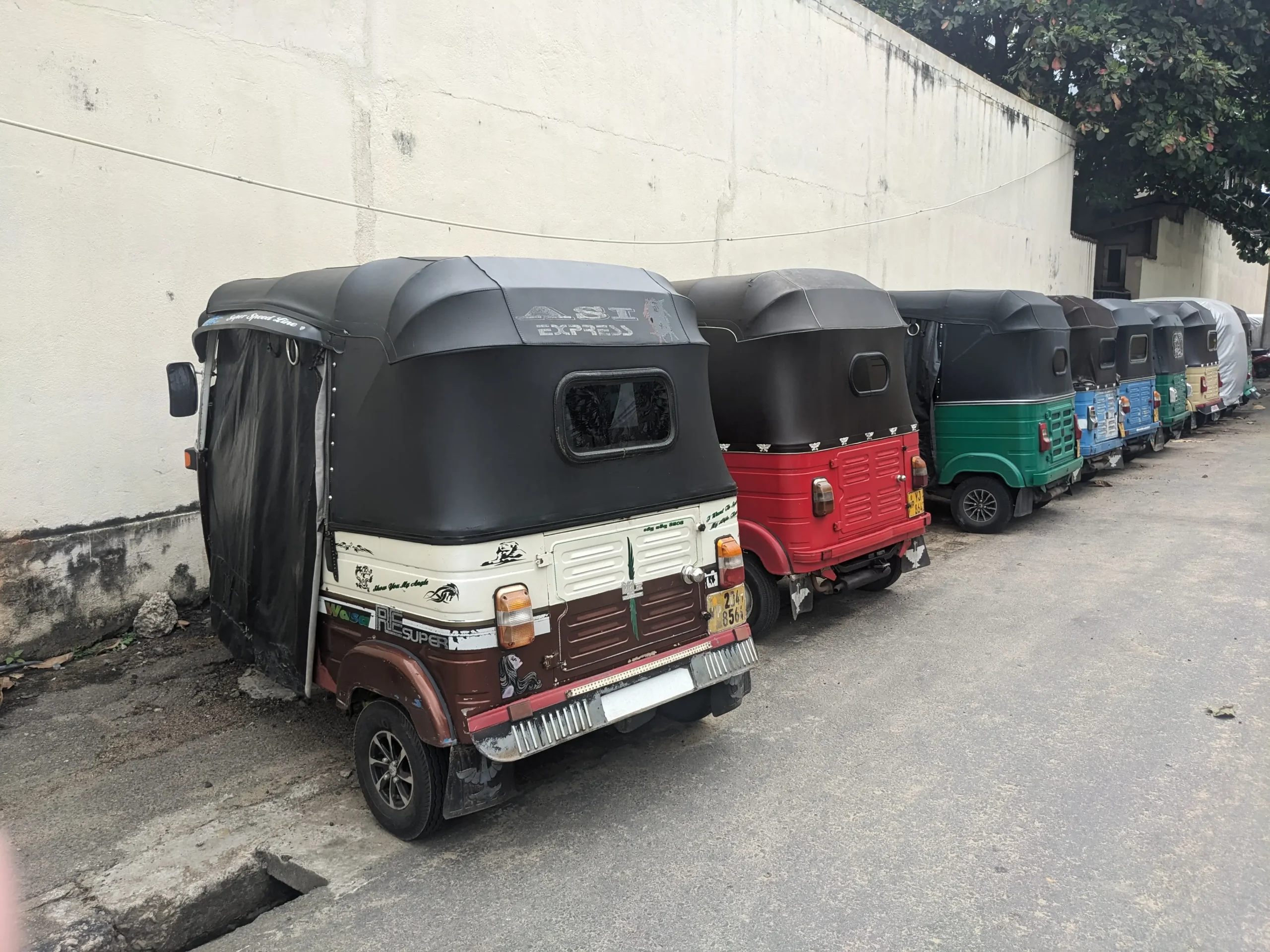 a row of tuktuks parked at the side of the road all in the different colours in Colombo, Sri Lanka