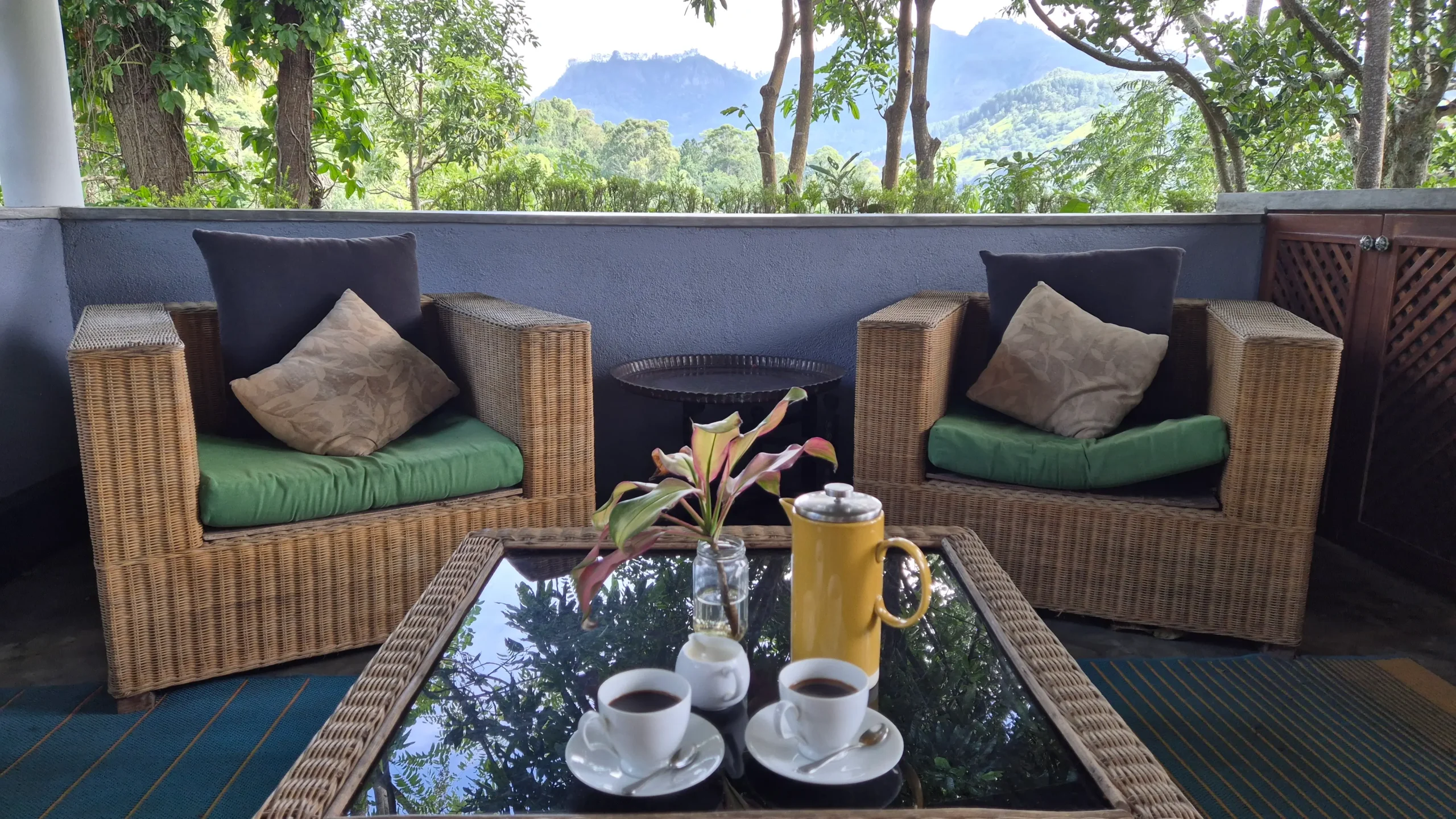 coffee with a view two cups of coffee, a coffee pot, and a small plant sit on a glass table with weaved rattan furniture, and a view over mountains of Sri Lanka