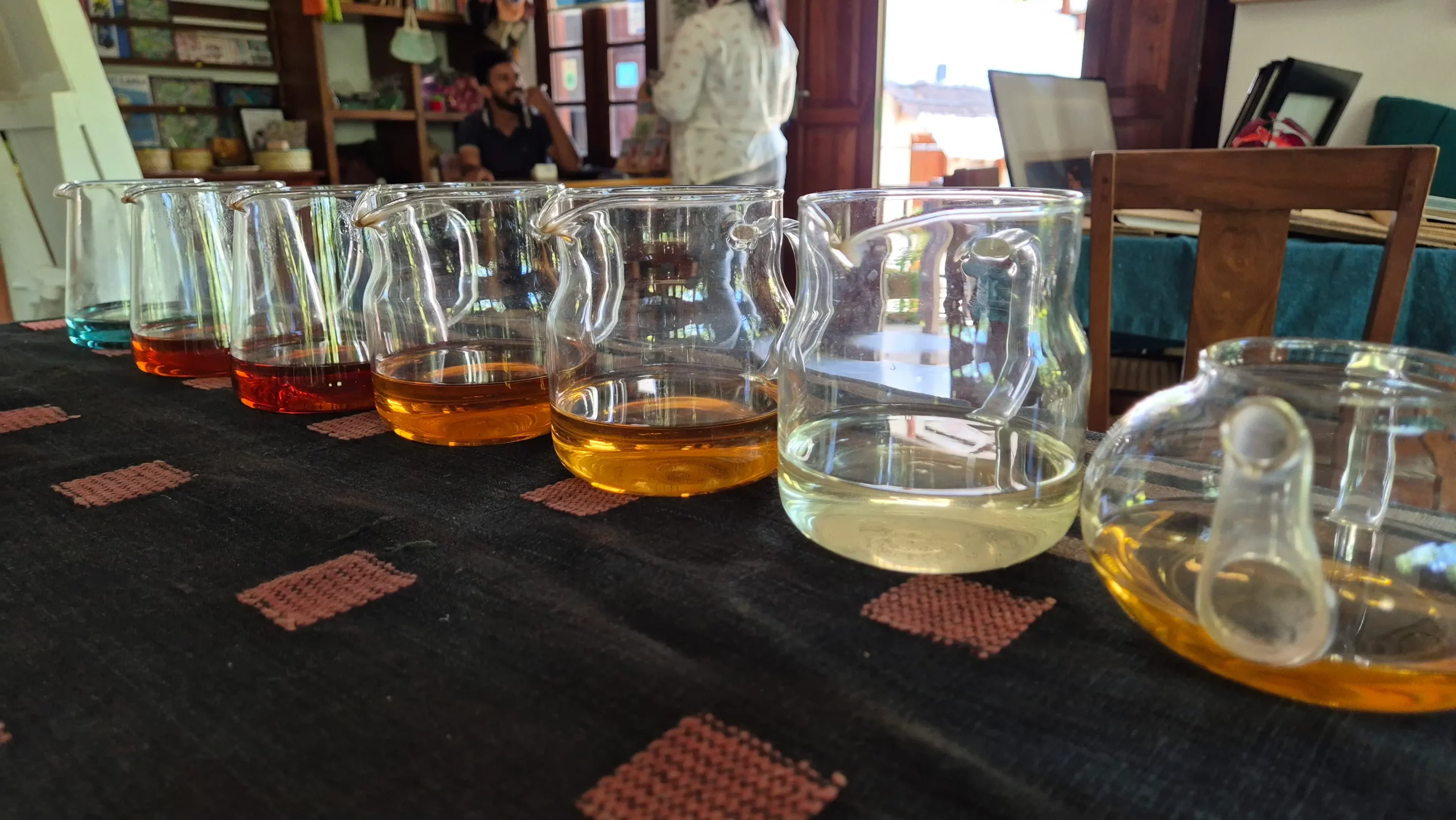 Amba Estate Tea Tasting six clear glass teapots are lined up next to each other each containing different types of Sri Lankan tea in different shades of yellow and orange