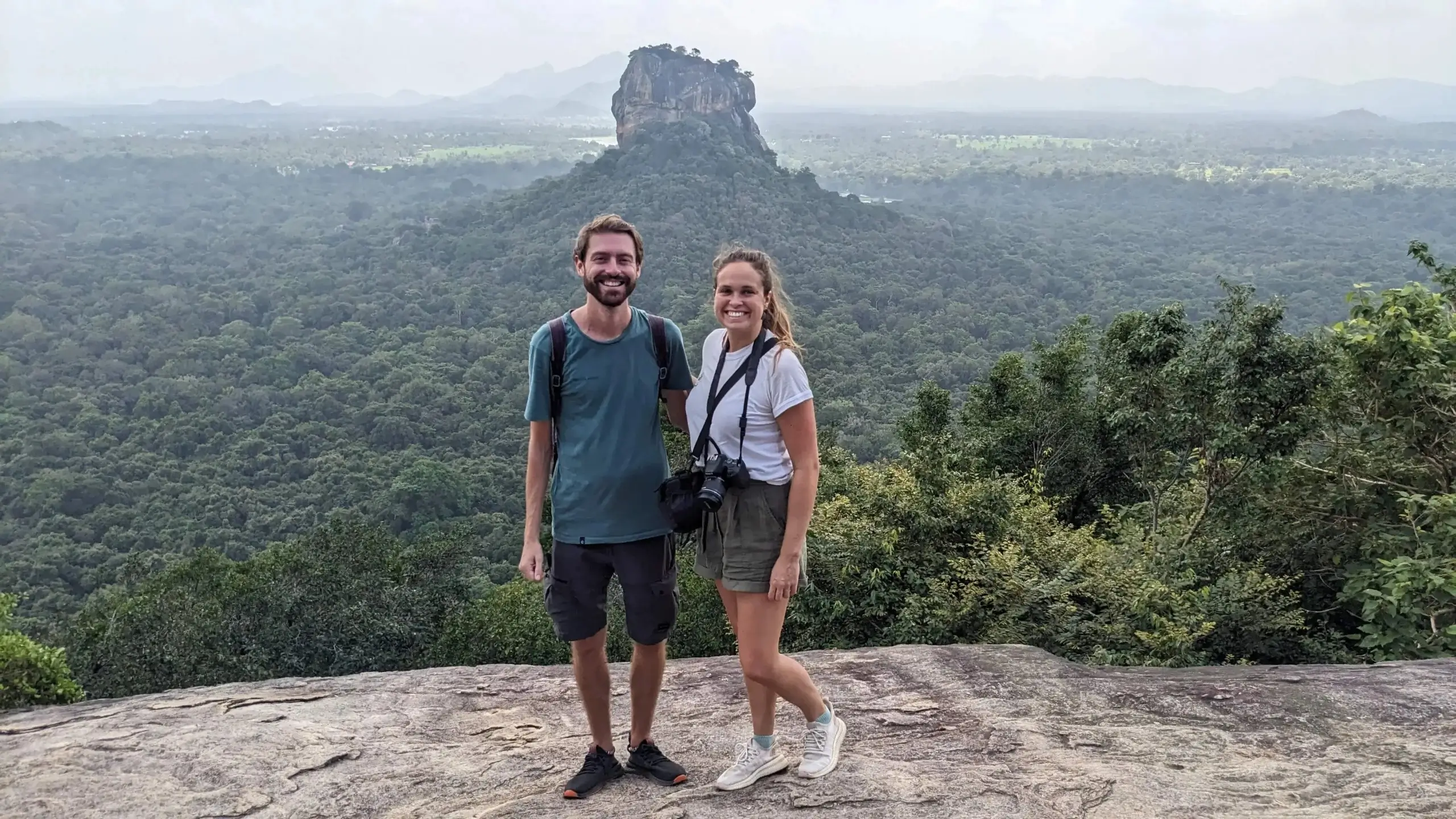 Pidurangala Rock viewpoint, Sri Lanka two people stand at Pidurangala Rock viewpoint with views over the green jungle of Sigiriya and Sigiriya Rock in the background - things to do in Sri Lanka