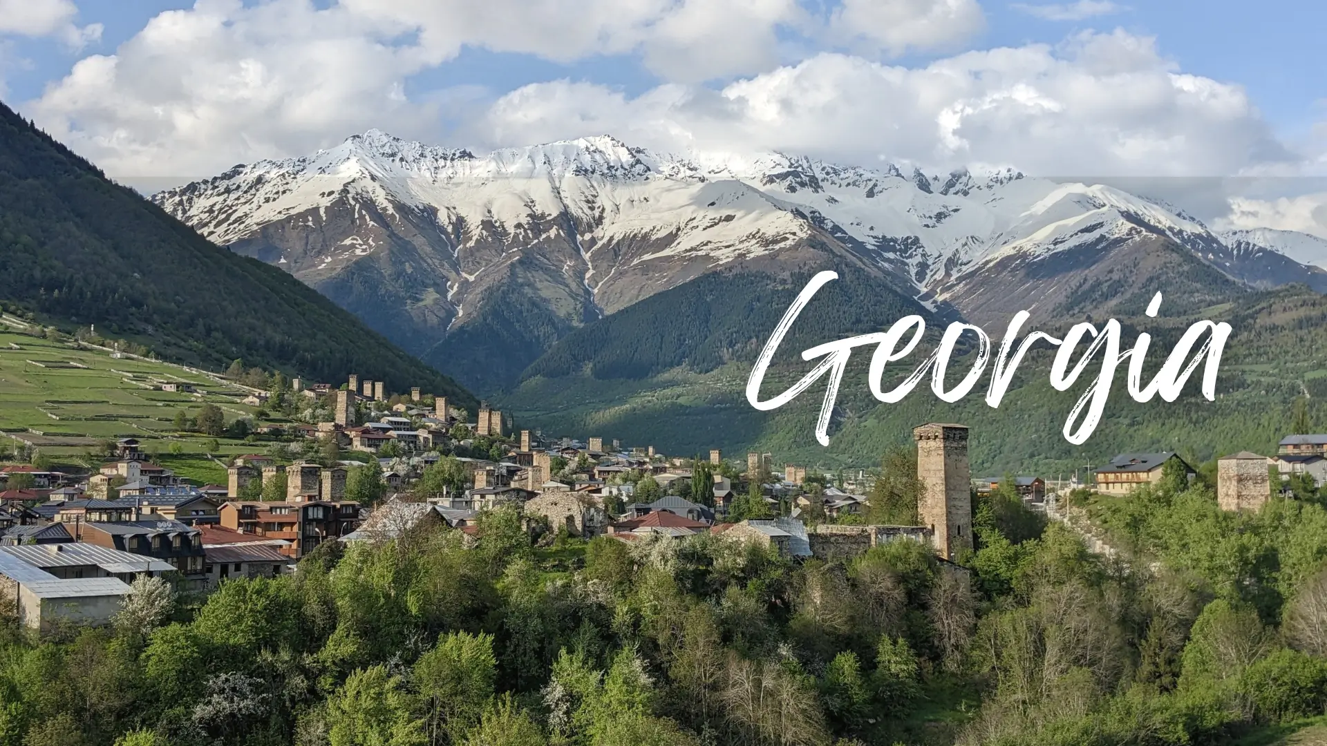 Georgia Travel Guide 7 snow-capped mountains in the background with a small mountain village dotted with medieval brick towers in the foreground - Mestia. Georgia travel guide