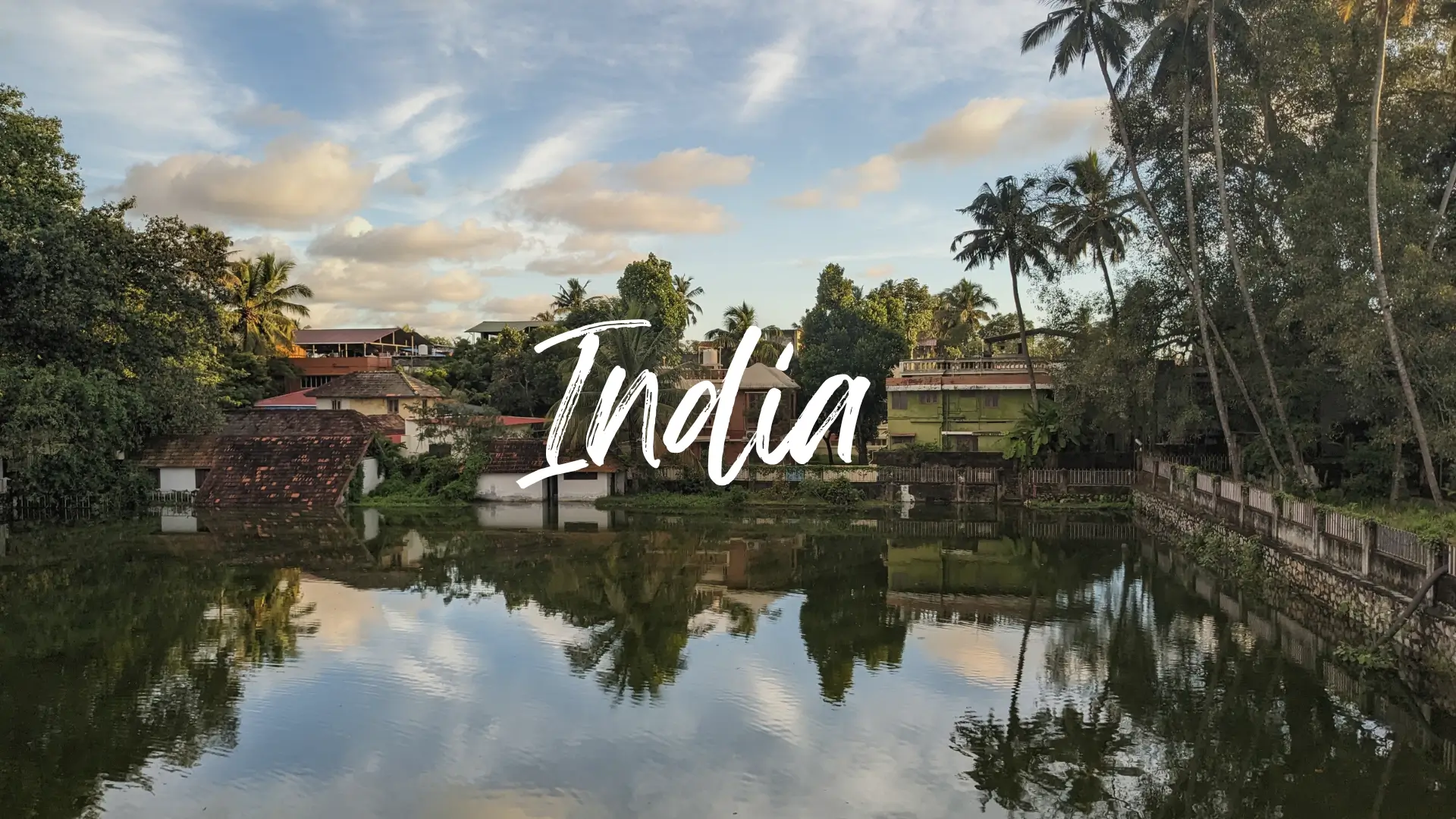 a pond has still water and reflects the surrounding buildings and palm trees. India travel guide