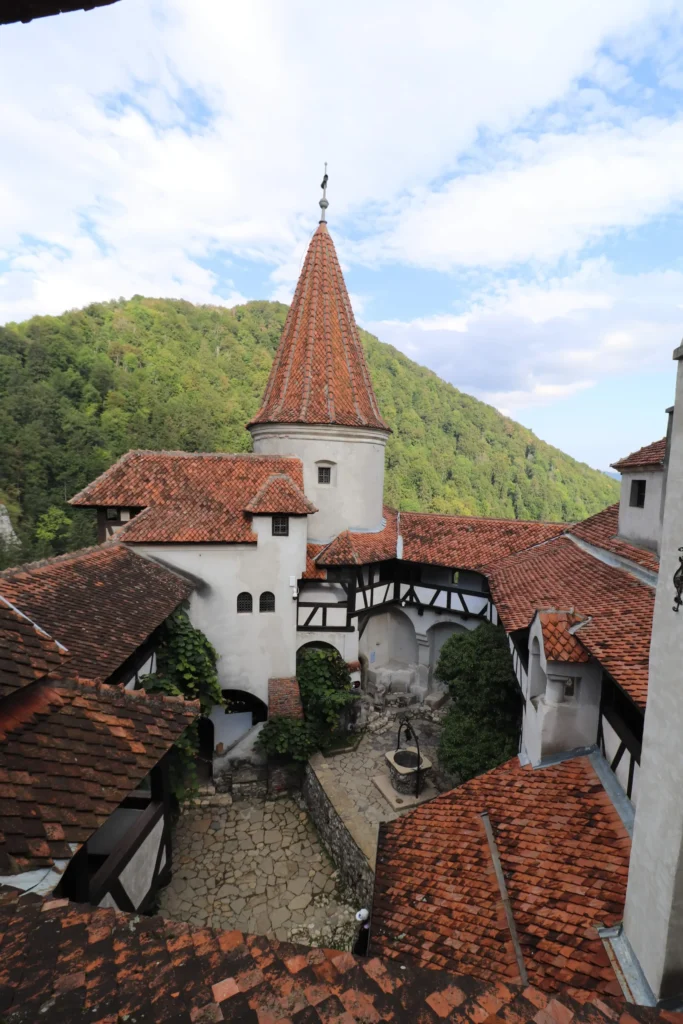 an internal courtyard has cobble stones, orange roof tiles, round turrets, pointed spires, exposed wooden beams against white walls at Bran Castle, Romania