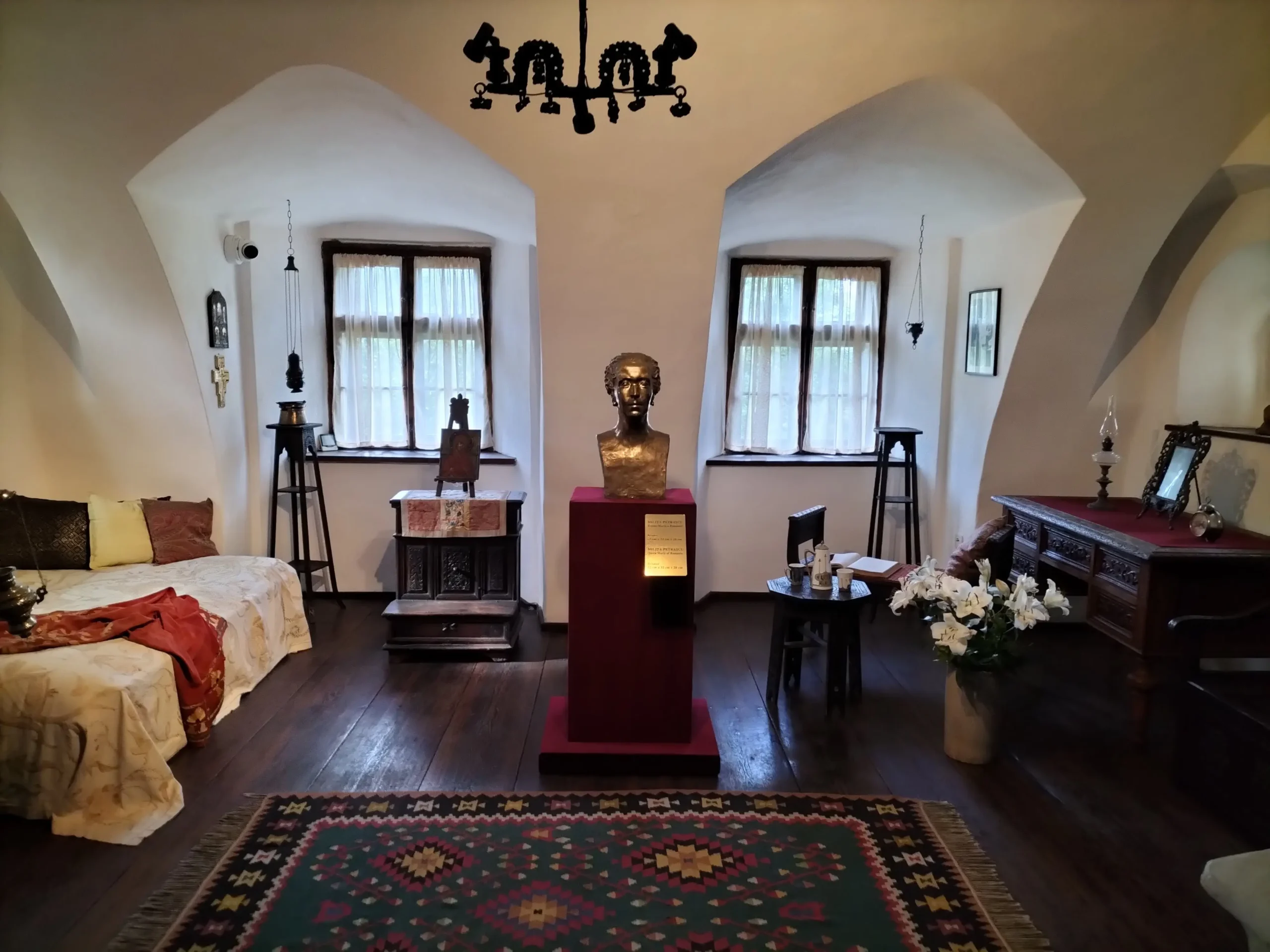 interior of Dracula's castle shows dark wooden floor boards, a traditional rug, dark wooden furniture, net curtains, and a bronze bust