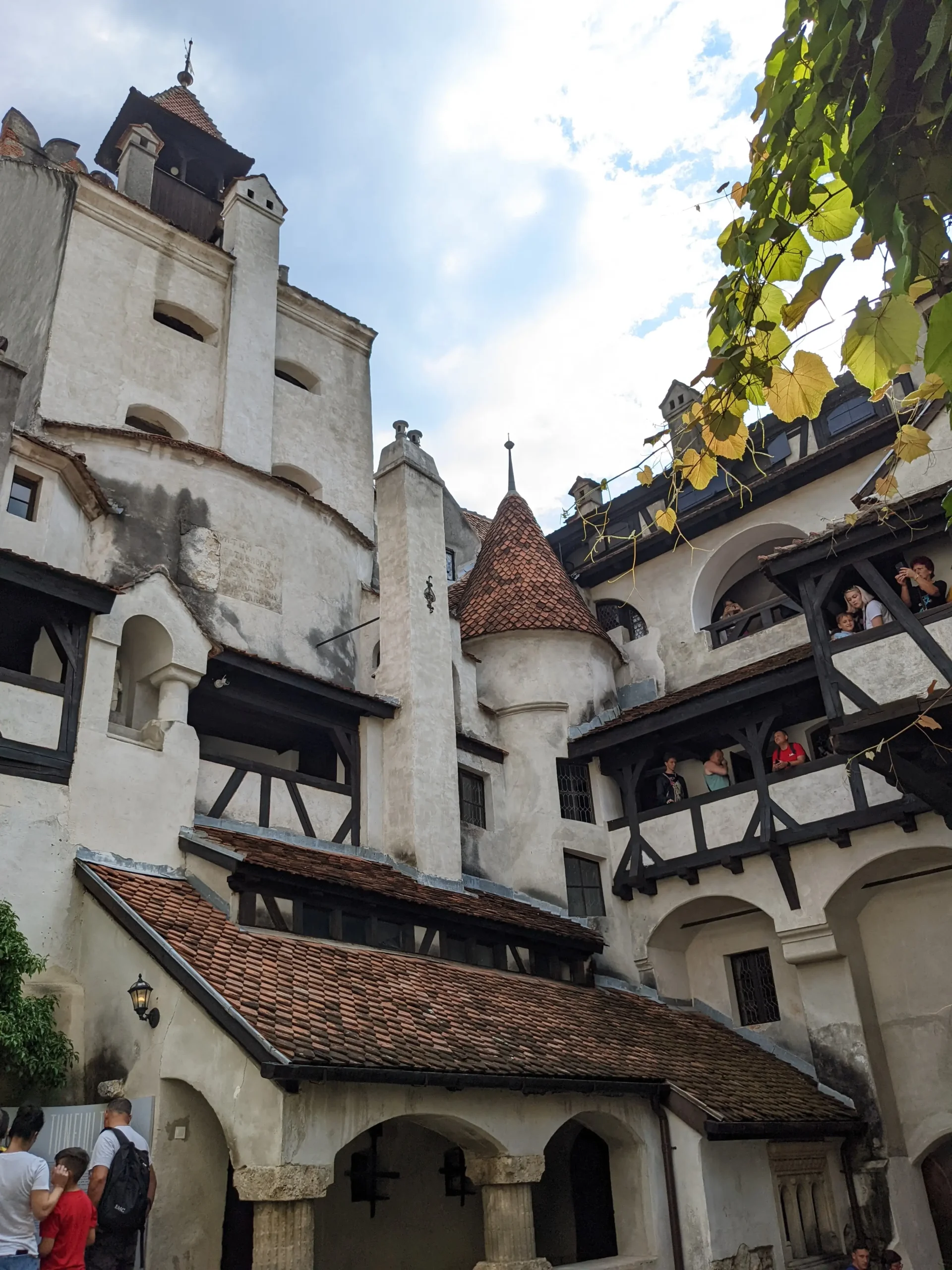 a courtyard at Bran Castle shows orange roof tiles, round turrets, tall spires, exposed wooden beams. Brasov to Bran Castle