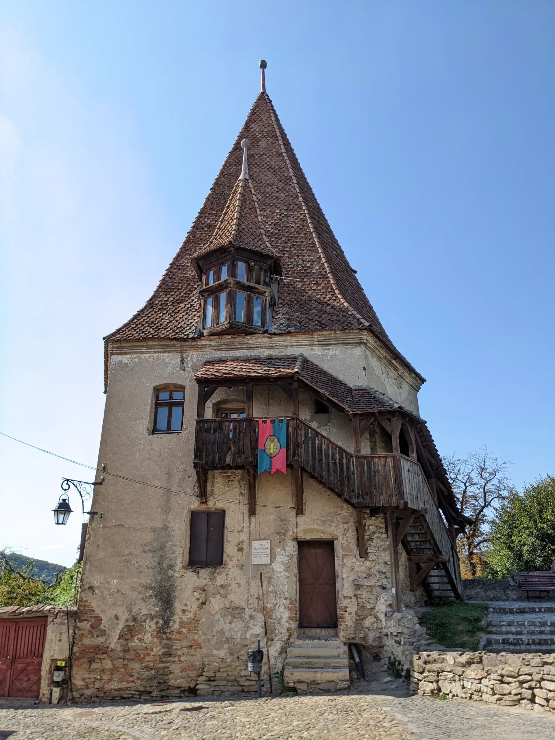 a brick tower has a covered wooden stair case around the outside, and a pointed tiled roof