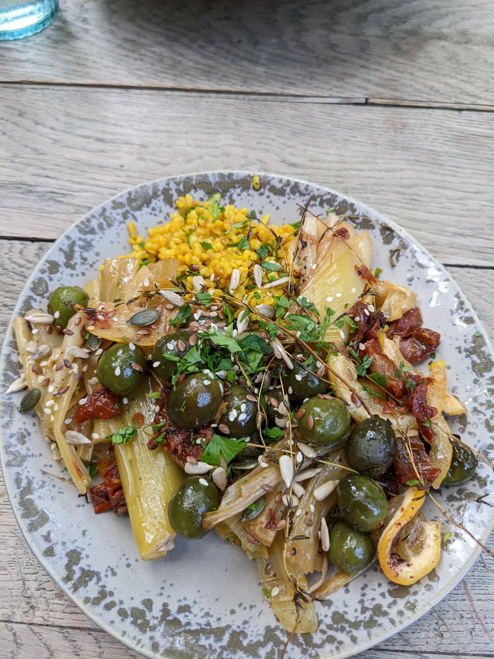 Manna Manna a plate of charred leeks, green olives, seeds, sundried tomatoes, yellow coucous and fresh herbs at Manna Manna in Brasov, Romania