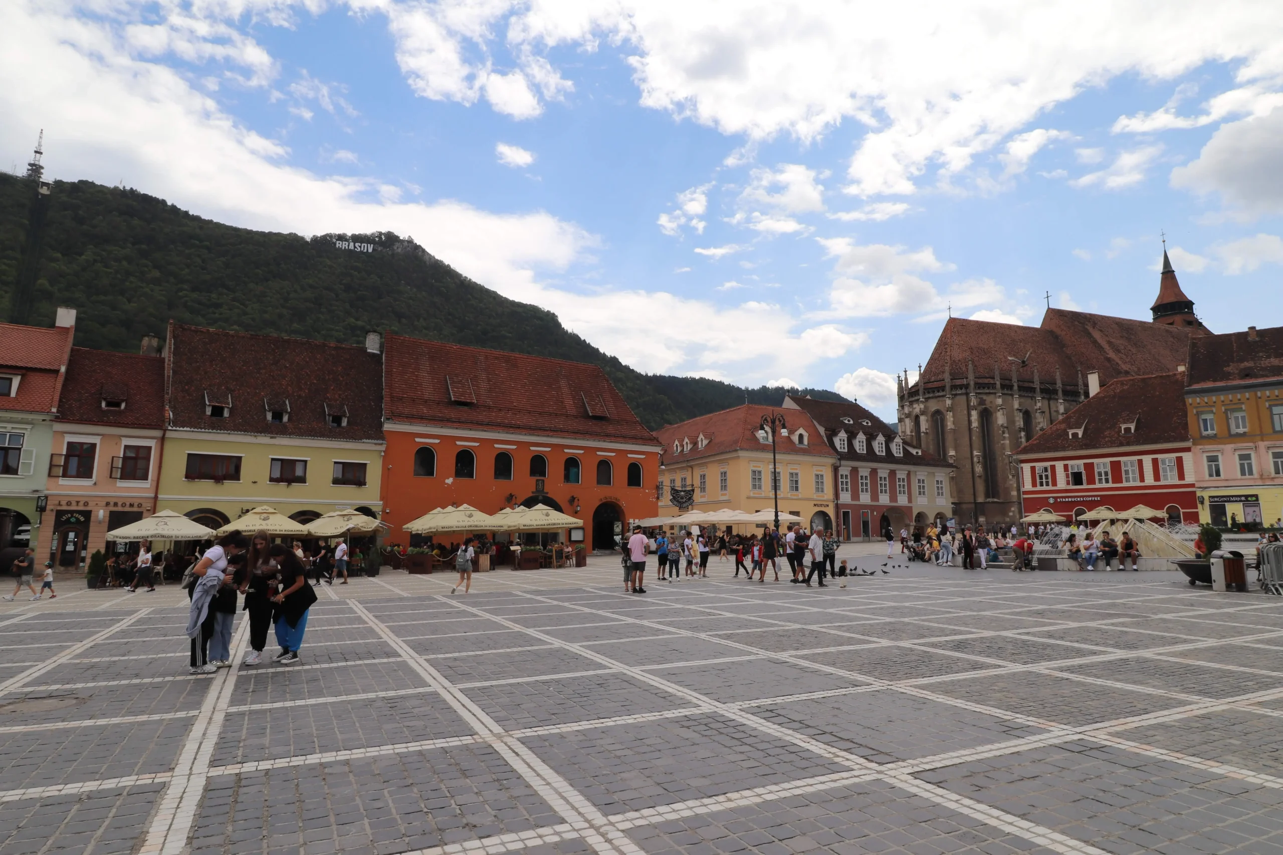 Piața Sfatului Piața Sfatului - Brasov's main square is lined with colourful buildings with brown/orange roof tiles.