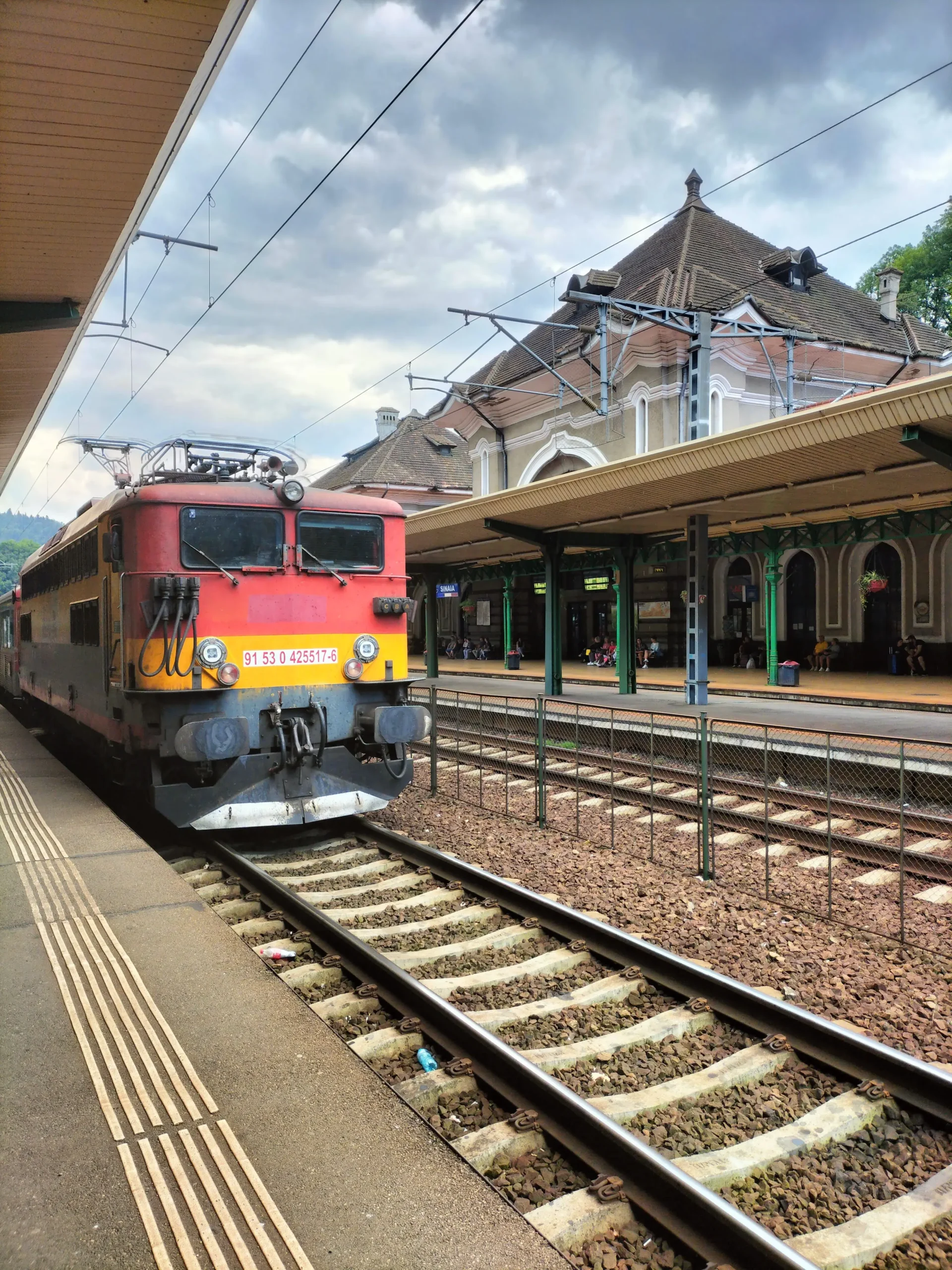 a red and yellow train pulls into a Romanian station - Bucharest to Brasov train