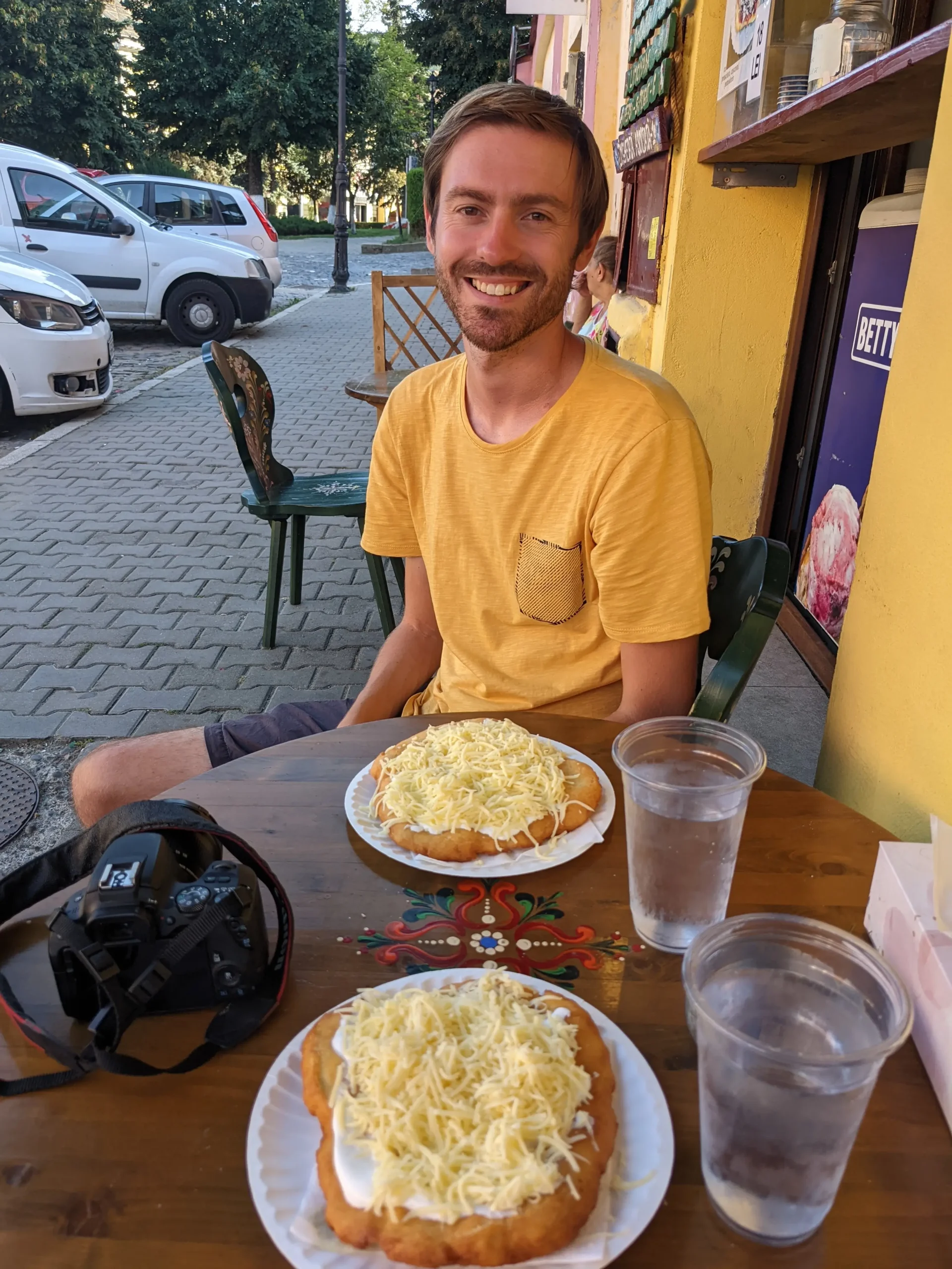 a man sits at a table with two plates of langos - a flat, savoury doughnut topped with sour cream and grated cheese