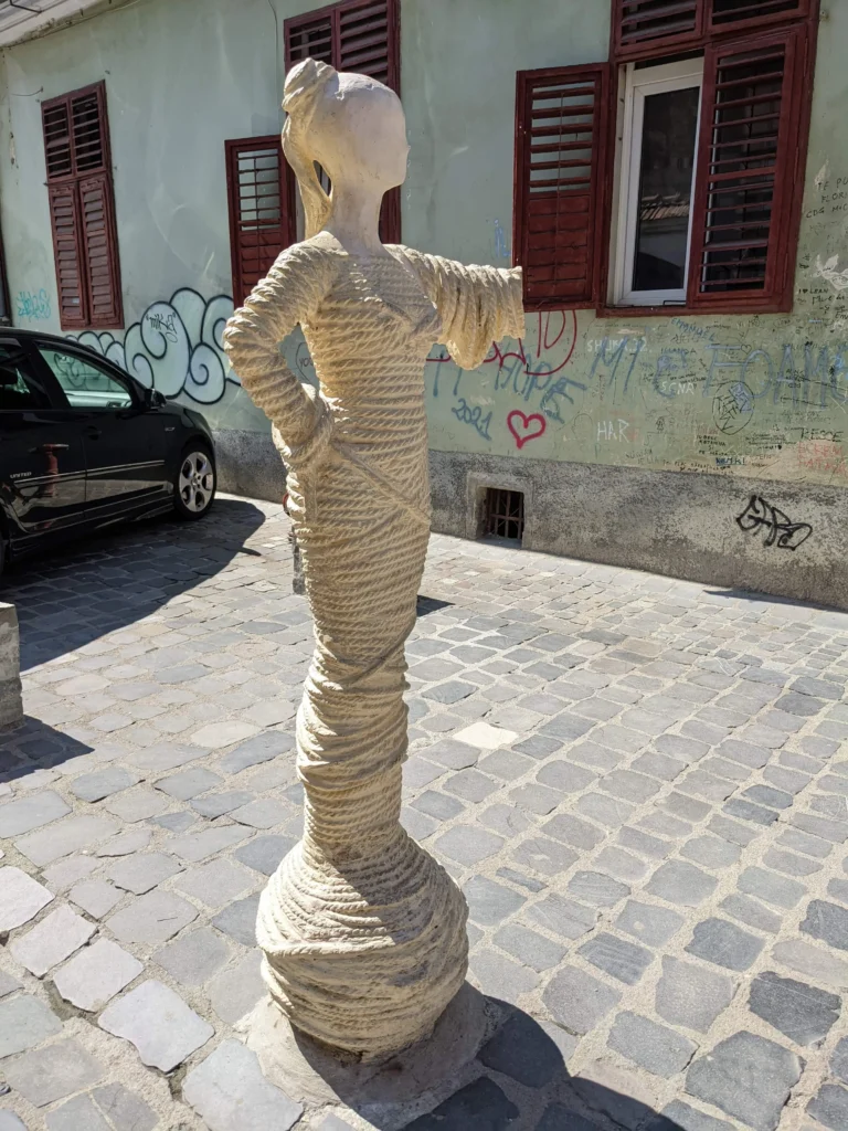 rope street sign Strada Sforii - a statue of a woman with rope wrapped around her points the way to Rope Street in Brasov, Romania
