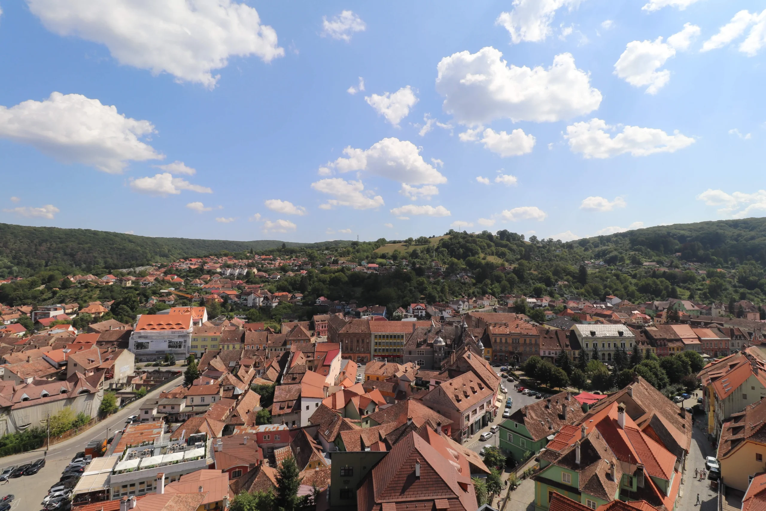 a view over a town of orange roof tiles and rolling green hills. Sighisoara